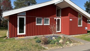 Un edificio rojo con puerta blanca, ventanas y un pequeño jardín con plantas y rocas.