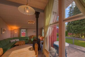 Interior acogedor de una cabaña con una mesa de comedor de madera, un sofá verde y un gran ventanal con vistas a un jardín.