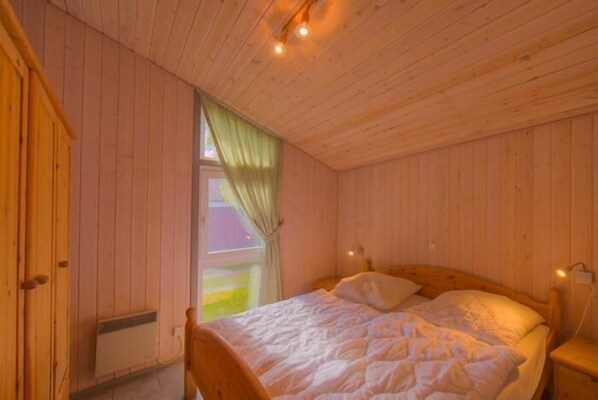 Una habitación acogedora de madera con una cama, un ventanal con cortinas y un radiador.