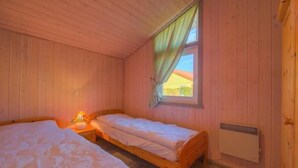A room with two wooden beds, a window with curtains, and a radiator.