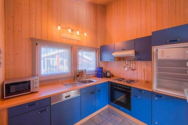 A compact kitchen with wooden walls, a microwave, a sink, and a dishwasher.