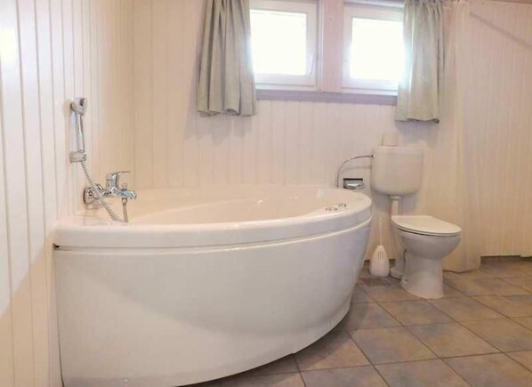 Ein Badezimmer mit freistehender Badewanne, Toilette und einem fenster mit Vorhängen.