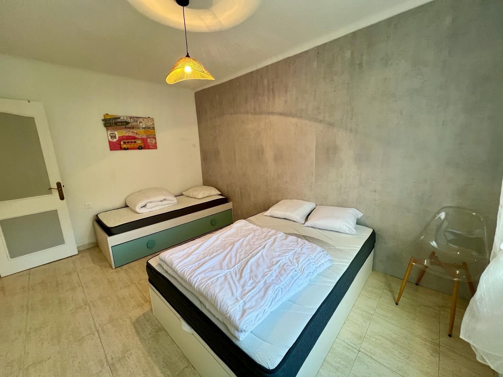 Een slaapkamer met twee bedden, een hanglamp, een poster aan de muur en een stoel.