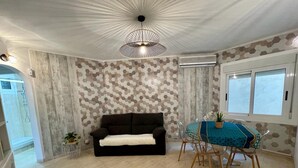 A living room with a black sofa, a dining table with chairs, a patterned wall, and a ceiling light fixture. - Port Cambrils 11004 (Cambrils)
