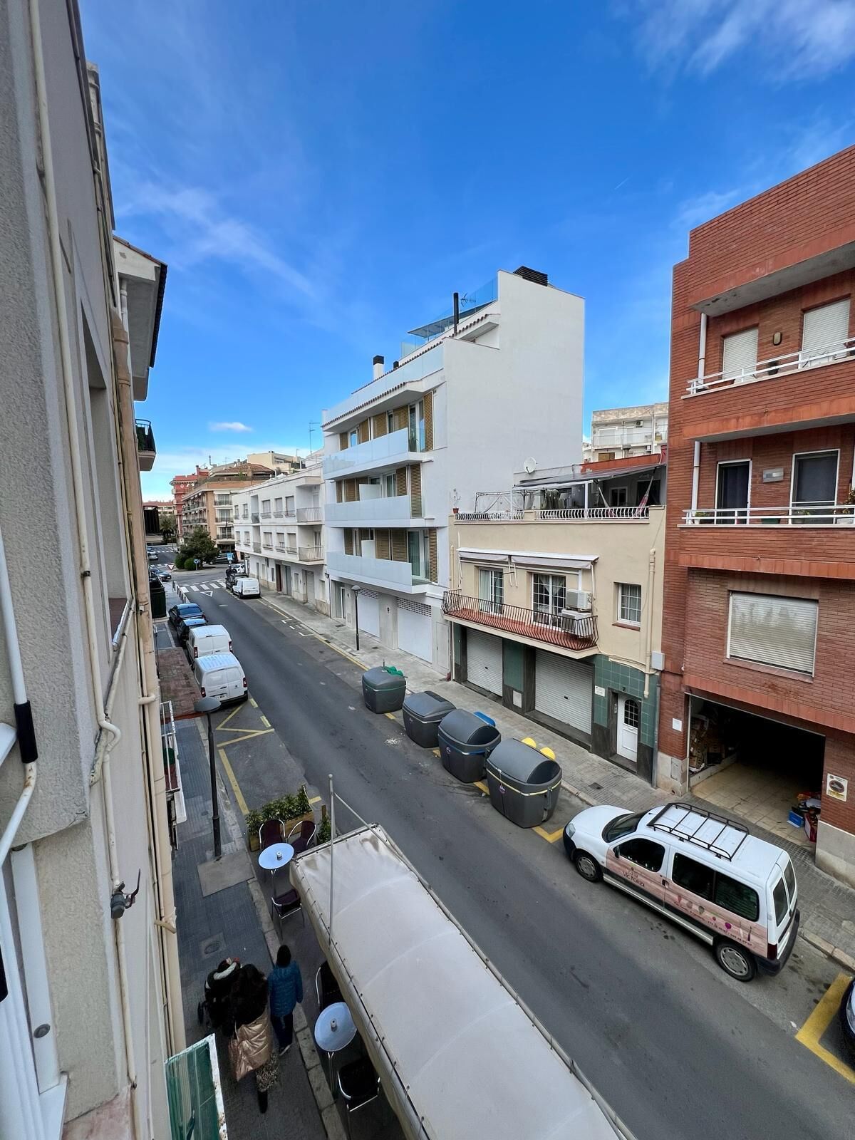 Une vue de rue avec des immeubles d’habitation, des voitures garées et un fourgon blanc sur la chaussée.