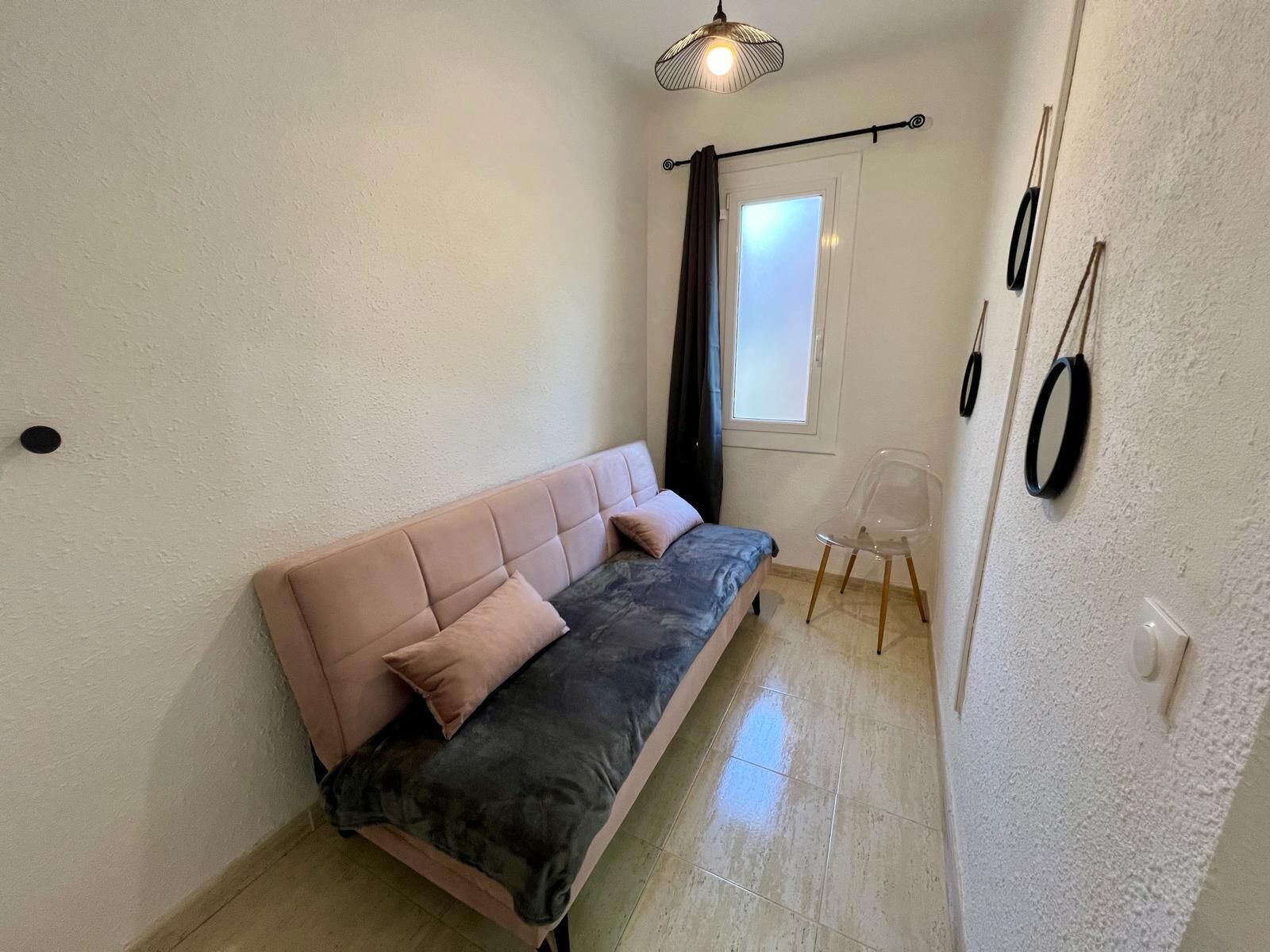 A small, well-lit room with a sofa, a chair, and a window with curtains.