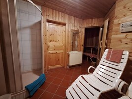 Interior de una cabaña de madera con sauna, zona de ducha y una silla reclinable con toalla.