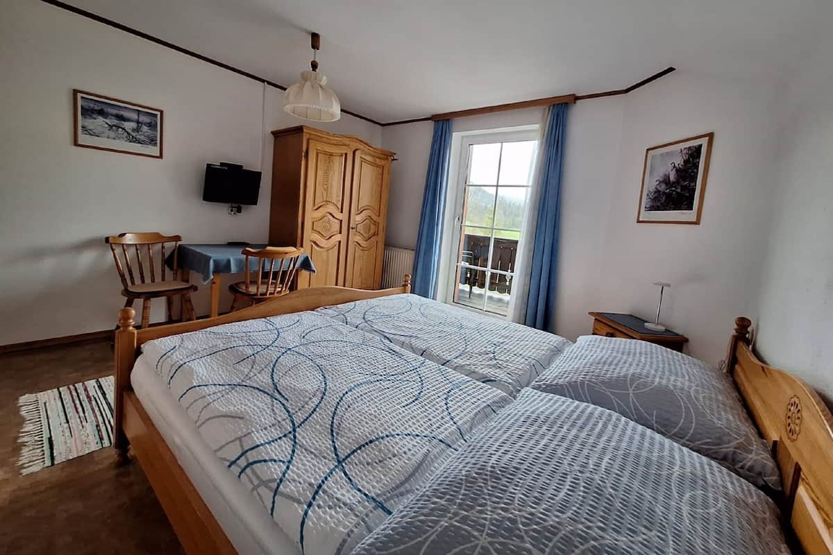 Ein Schlafzimmer mit einem großen Bett, einem Holzschrank, einem Schreibtisch mit Stuhl, einem Fernseher und einem Fenster mit Vorhängen.