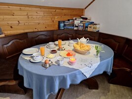 Una mesa de comedor dispuesta con alimentos para el desayuno, rodeada de paneles de madera y libros en un estante.