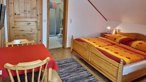 Ein Schlafzimmer mit einem hölzernen Bett, einem roten Tisch, einem Stuhl, einem Streifen Teppich und einer Holztür.