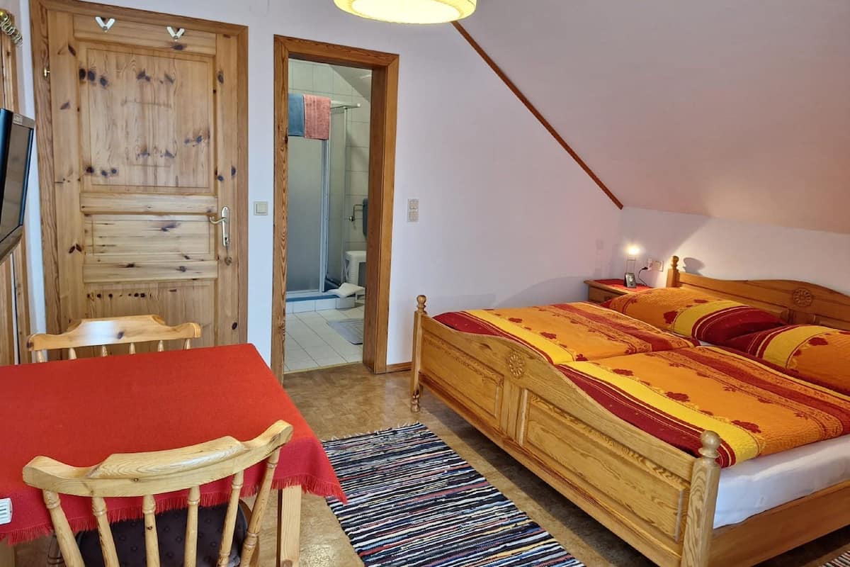 Ein Schlafzimmer mit einem hölzernen Bett, einem roten Tisch, einem Stuhl, einem Streifen Teppich und einer Holztür.