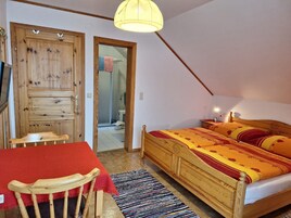 Un dormitorio con una cama de madera, una mesa roja, una silla, un tapete a rayas y una puerta de madera.