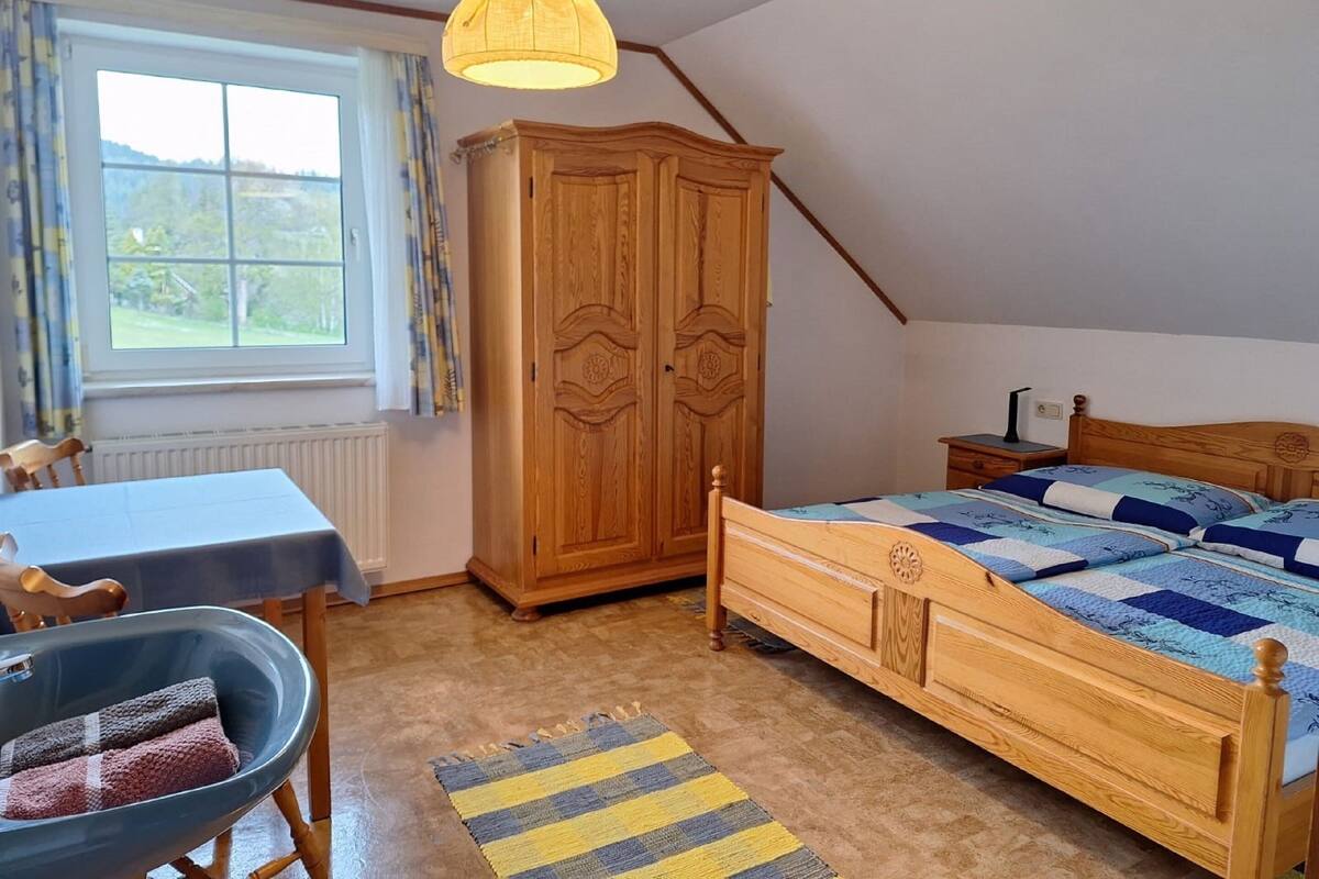 Ein Schlafzimmer mit einem hölzernen Bett, einem Tisch mit Stuhl, einem Kleiderschrank und einem Fenster mit Vorhängen.