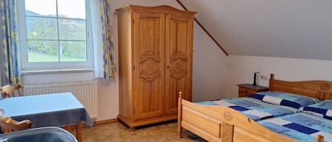A bedroom with a wooden bed, a table with a chair, a wardrobe, and a window with curtains.