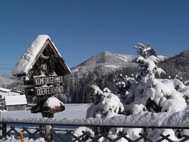 Una cabaña de madera con un letrero que indica que es un "Komfortzimmer Oberfeichtner" en una zona montañosa nevada.