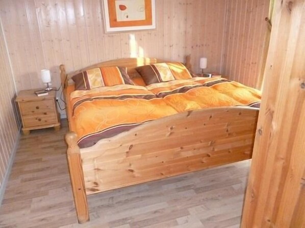 Una cama de madera con un edredón estampado, una mesita de noche con una lámpara y un cuadro en la pared.