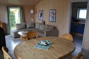 A cozy room with a wooden floor, a round wooden table, a grey sofa, and a kitchen area with blue cabinets.