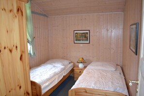 A room with two wooden beds, a small bedside table with a lamp, and a framed picture on the wall.
