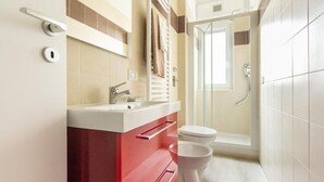 A modern bathroom with a red vanity, a white sink, a toilet, and a glass shower enclosure.