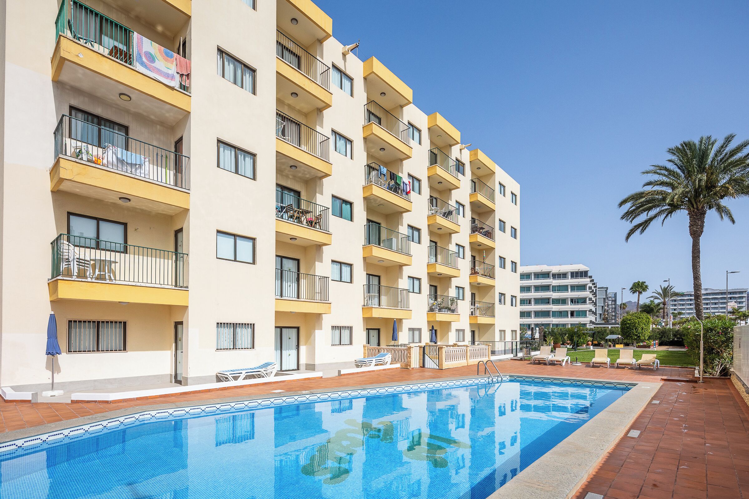 A hotel with a swimming pool, multiple balconies, and a palm tree.