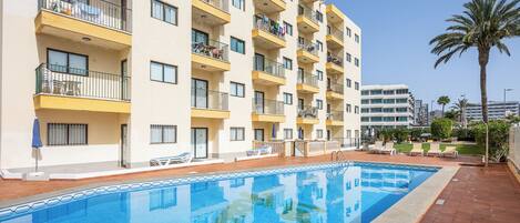 A hotel with a swimming pool, multiple balconies, and a palm tree.