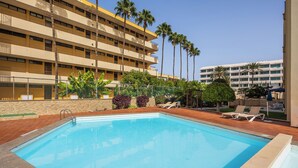 A hotel with a swimming pool, palm trees, and lounge chairs. - Apartamento Los Ficus (San Bartolomé de Tirajana)
