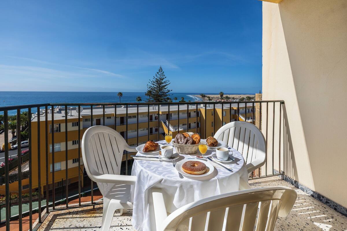 A balcony with a table set for breakfast, overlooking a beach and ocean.
