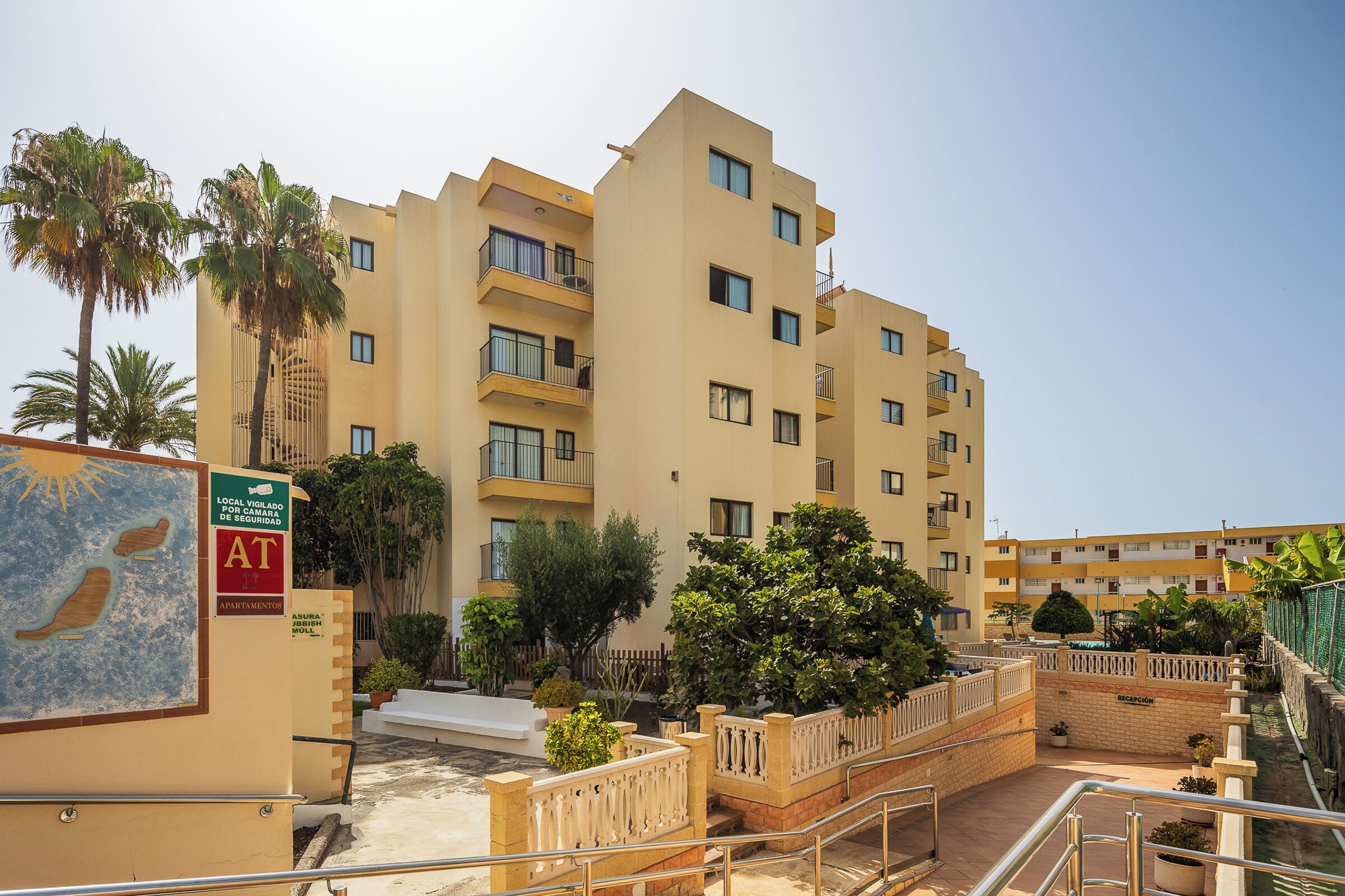 A multi-story hotel with balconies, a reception area, and a landscaped courtyard with palm trees.