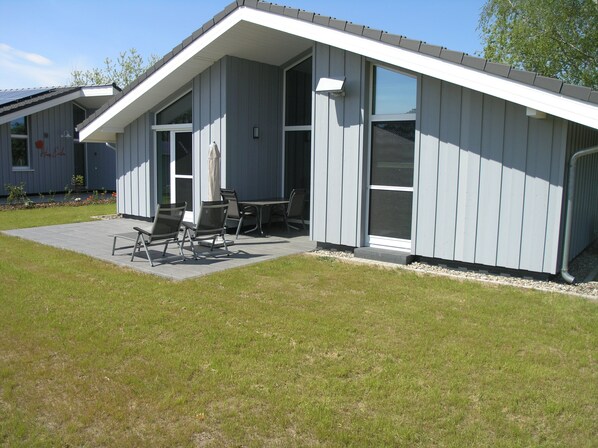 A residential building with a covered patio area, outdoor seating, and a well-maintained lawn.
