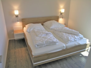 A double bed with white bedding, two bedside tables, and wall-mounted lamps. - Seeschwalbe 324 - Das Skandinavische Familienhaus für 4 mit Sauna und Whirlpool (Mirow)