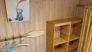 Una habitación con paredes de madera, un estante blanco con ganchos, un banco de madera y un amplio armario de madera con varios cajones.