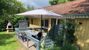Un patio con una mesa y sillas, un horno de ladrillo pequeño y un edificio amarillo con tejado de azulejos.