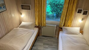 Una habitación con dos camas individuales, paredes de madera, un radiador y una ventana con cortinas.