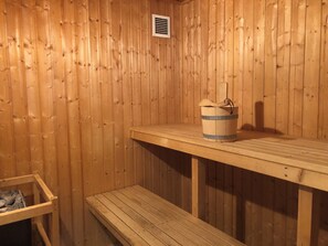 En träbeklädd bastu med en bänk, en träspänd hink och ett ventilationsgaller.