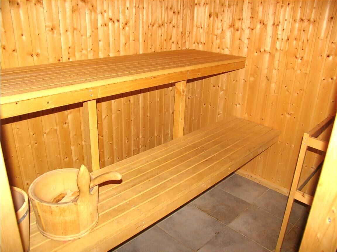Een houten sauna met een bank, een houten emmer en een houten stoel.