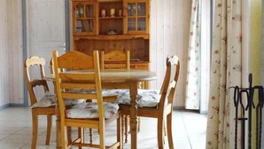 Un comedor con una mesa y sillas de madera, un mueble con puertas de cristal y una cortina con motivos florales.