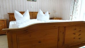 Una cama de madera con ropa de cama blanca en una habitación con paredes de madera y una cortina con motivos florales.