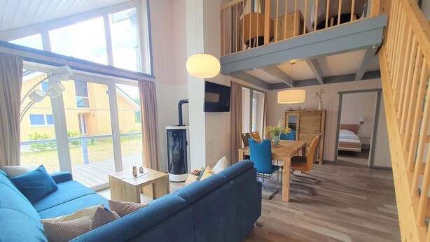 Ein geräumiger Wohnbereich mit blauem Sofa, Holzboden, einem Esstisch mit Stühlen und einem Schlafbereich im oberen Bereich mit Holzbalkon.