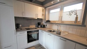 A modern kitchen with white cabinets, a built-in oven, a sink, and a window with a plant.