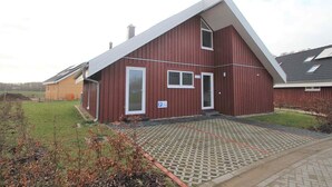 A red two-story house with a sloped roof, a paved driveway, and a small garden area.
