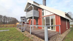 A modern two-story house with a wooden deck, large windows, and a chimney.