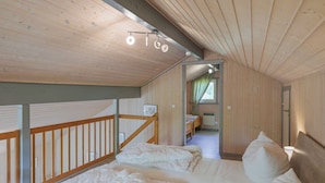 A wooden cabin with a loft bedroom, a balcony with a railing, and a small bathroom visible through a doorway.