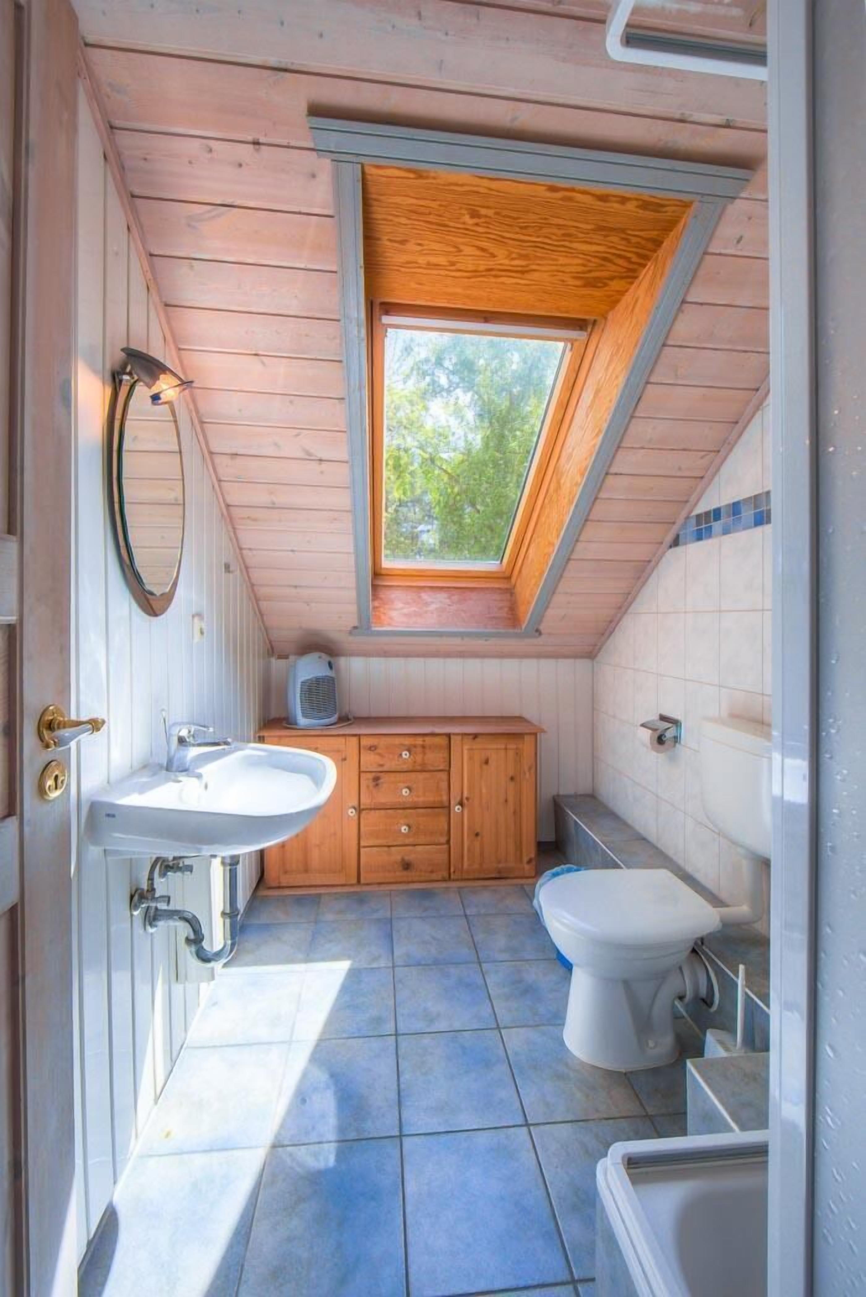 Et lille badeværelse med ovenlys, vask, toilet og badekar.