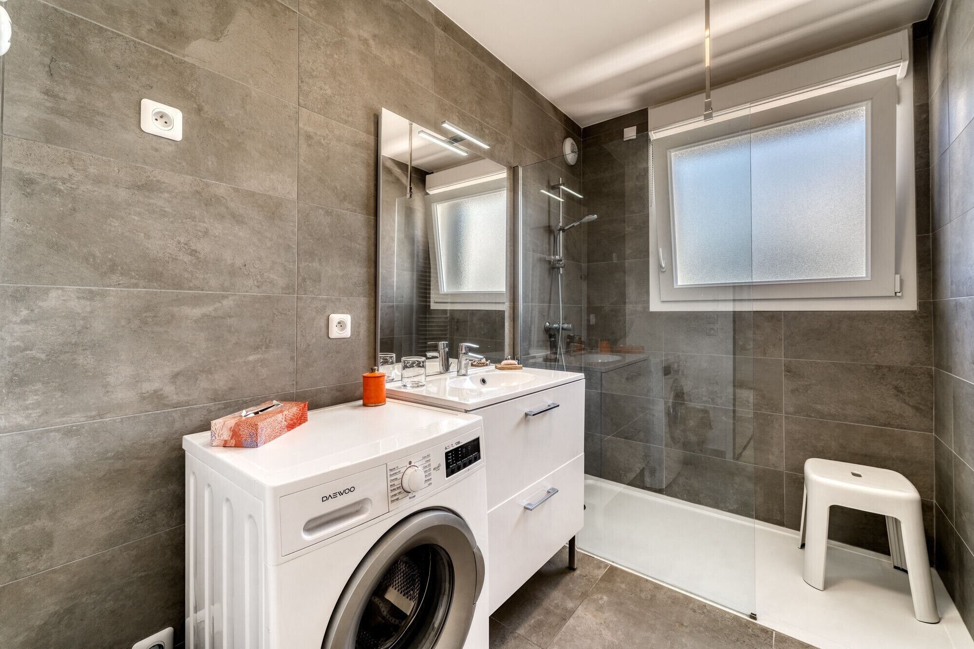 Ein modernes Badezimmer mit Waschmaschine, Waschbecken und Dusche.