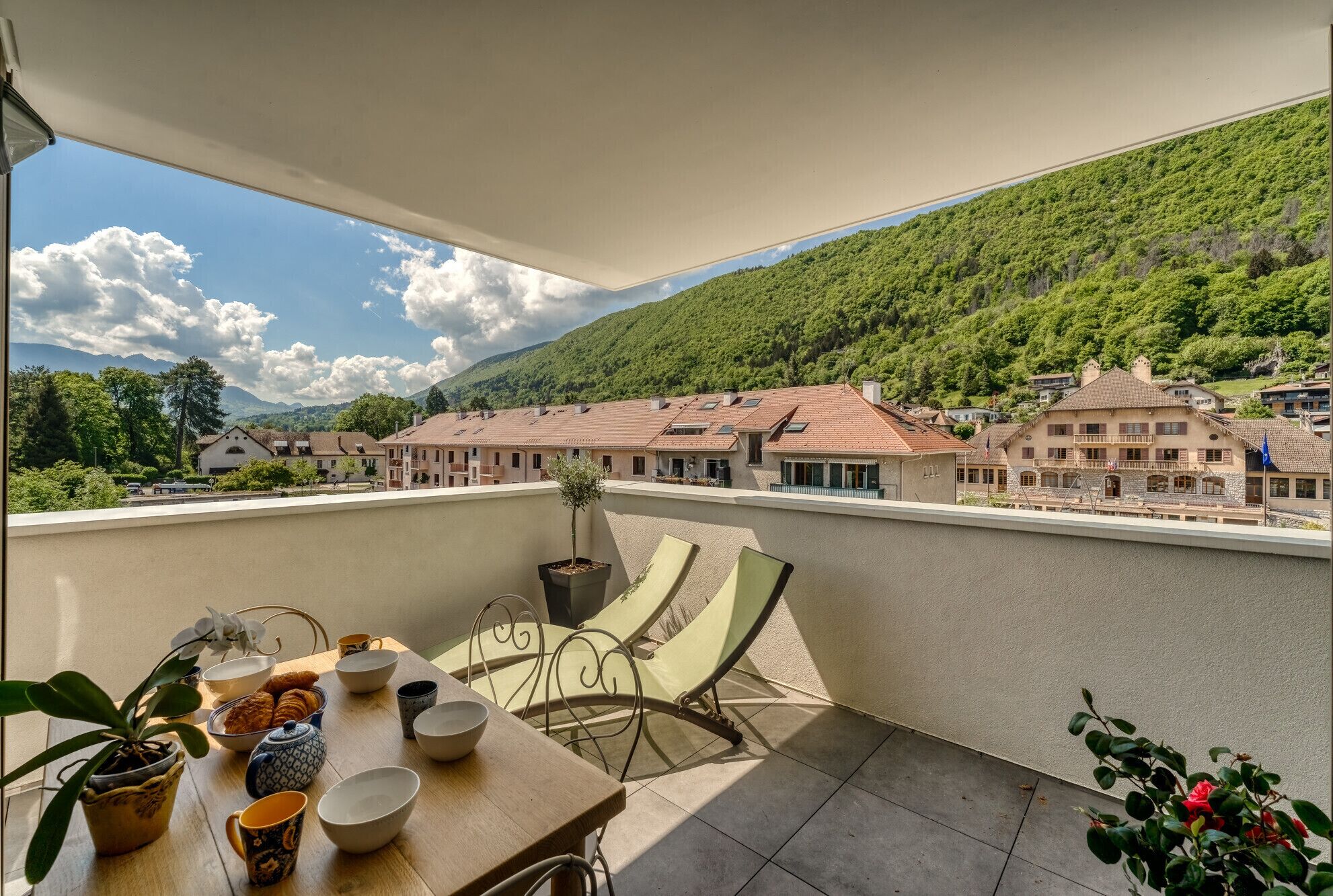 Ein Balkon mit Frühstückstisch, mit Blick auf ein Dorf mit traditionellen Gebäuden und einem Berg im Hintergrund.