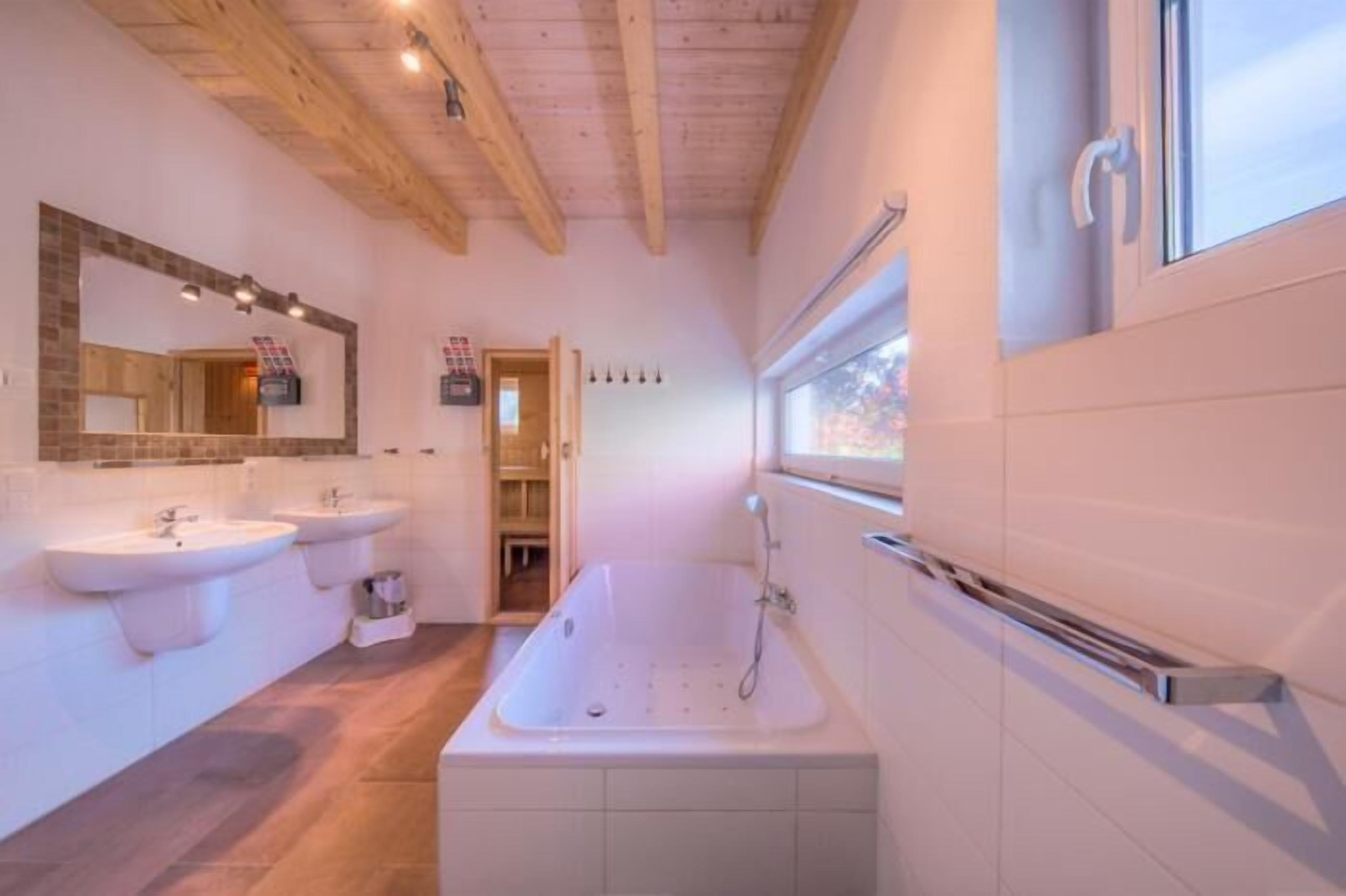 Un baño moderno con dos lavamanos, una bañera grande y un ventanal que proporciona luz natural.