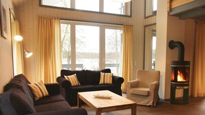 Een gezellige woonkamer met een open haard, twee banken, een houten bijzettafeltje en grote ramen.