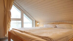 Een slaapkamer met een houten bed, grote ramen en een schuin dak.