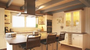 Een moderne keuken met een centraal eiland, barkrukken, witte kasten en een inbouwoven.