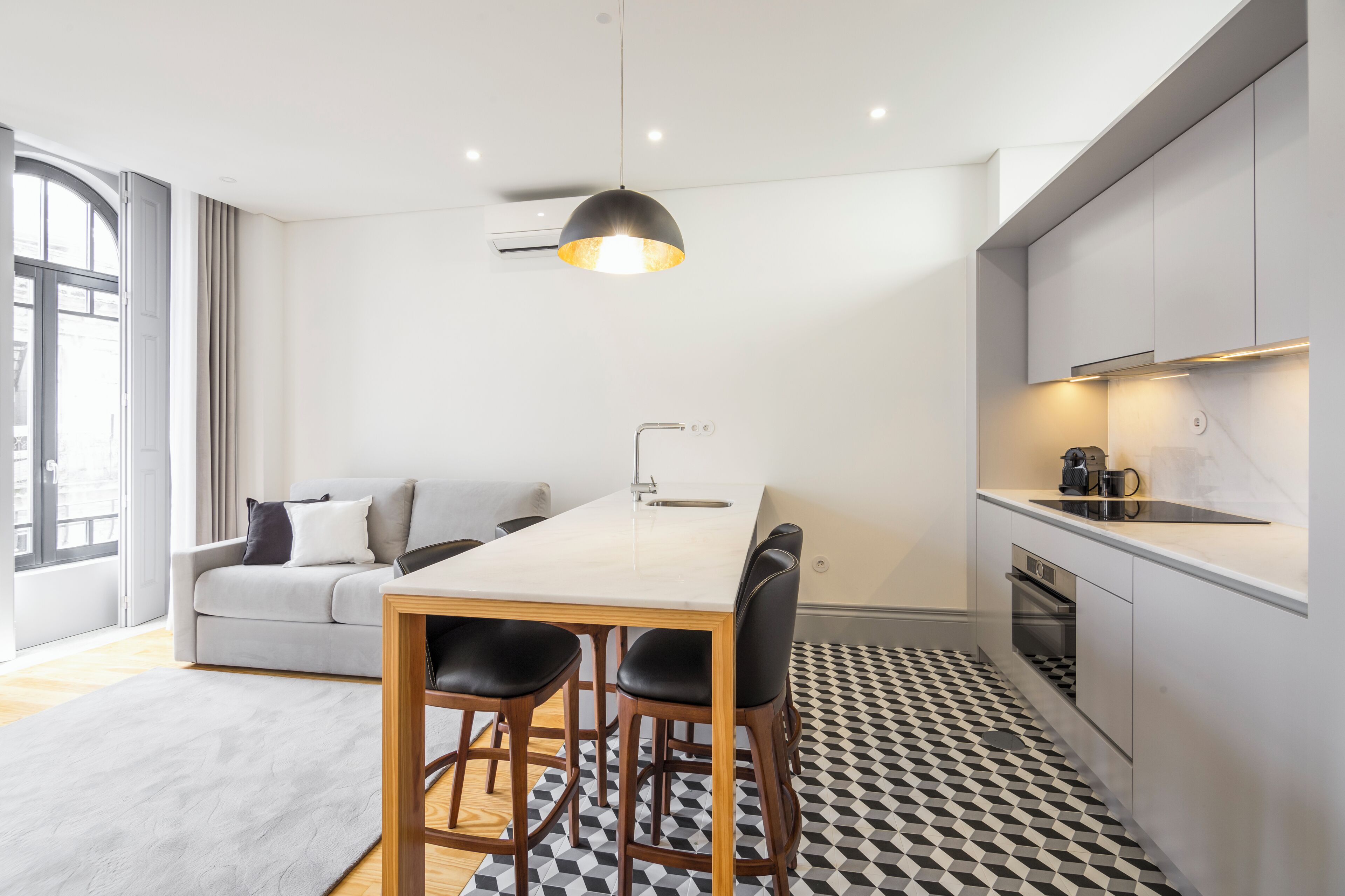Una cucina moderna con zona pranzo, caratterizzata da un tavolo bianco, pavimento a motivi bianchi e neri e un divano grigio.